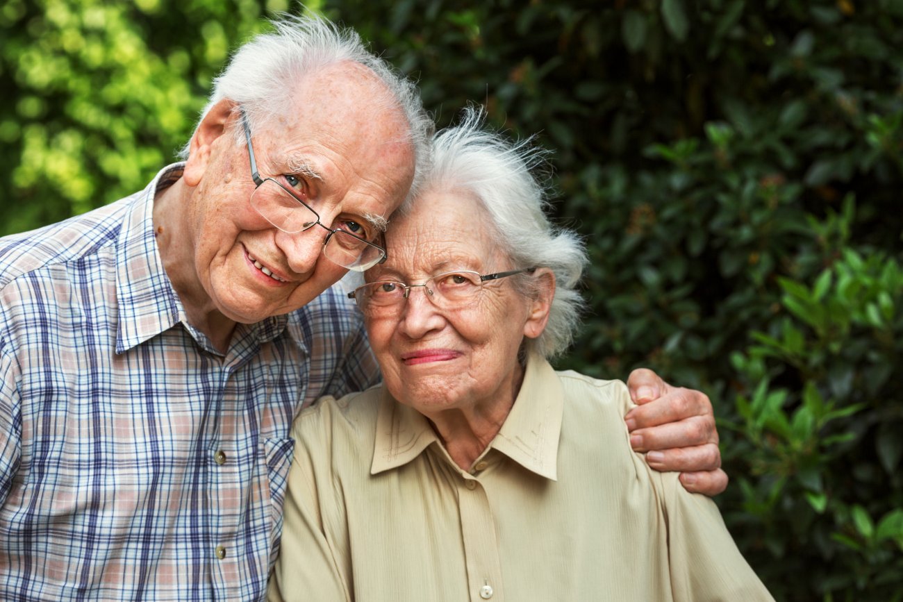 Un homme et une femme âgées se tiennent par l'épaule en souriant
