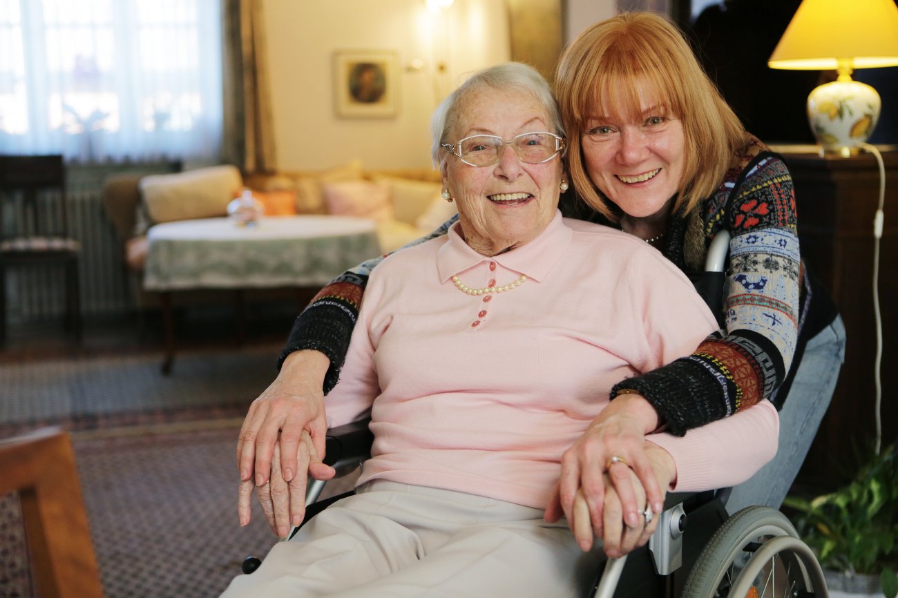 Une femme âgée est assise dans un fauteuil roulant et une femme plus jeune la tient dans ses bras.