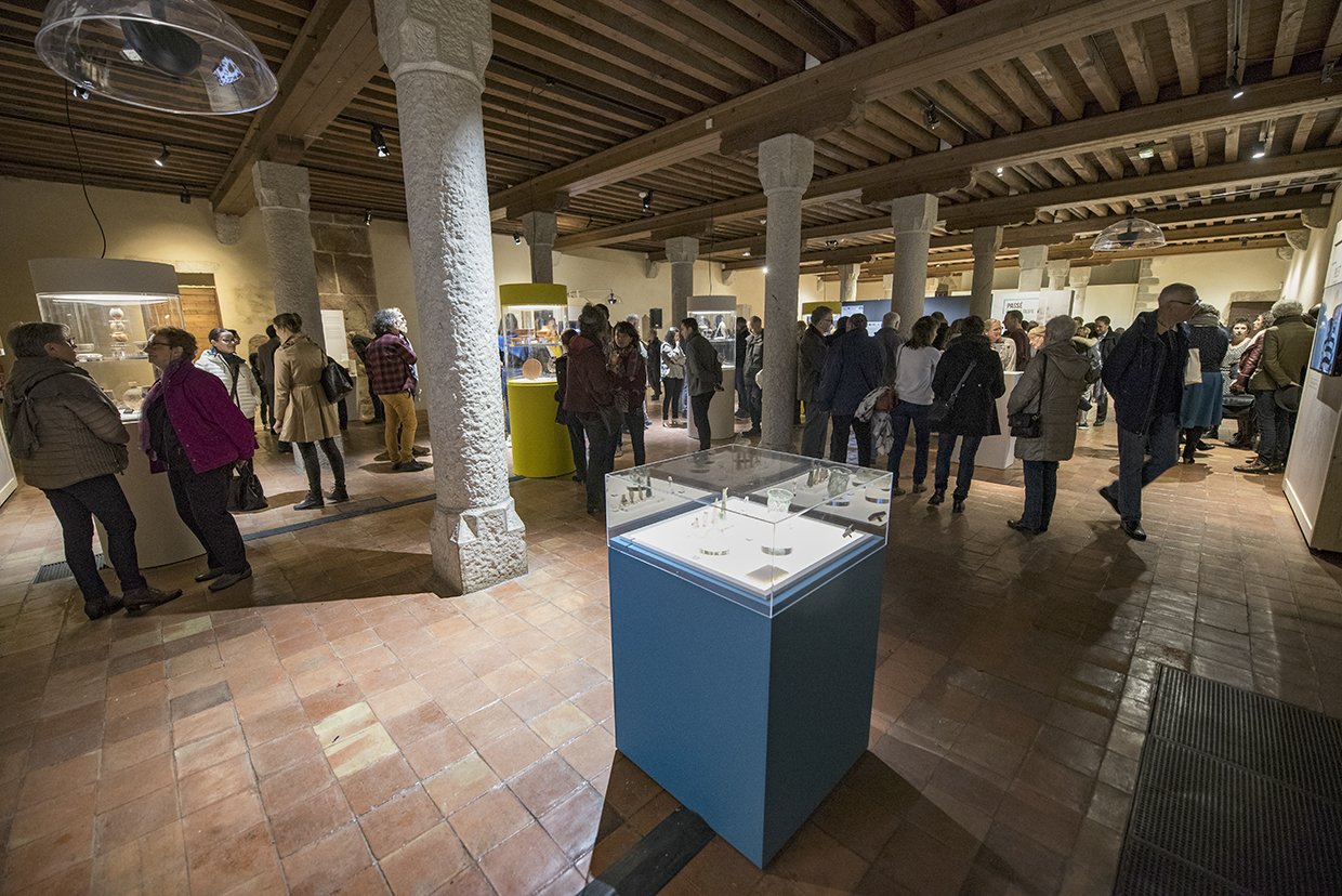 Des personnes visitent une exposition dans une salle au plafond en bois soutenu par des colonnes.