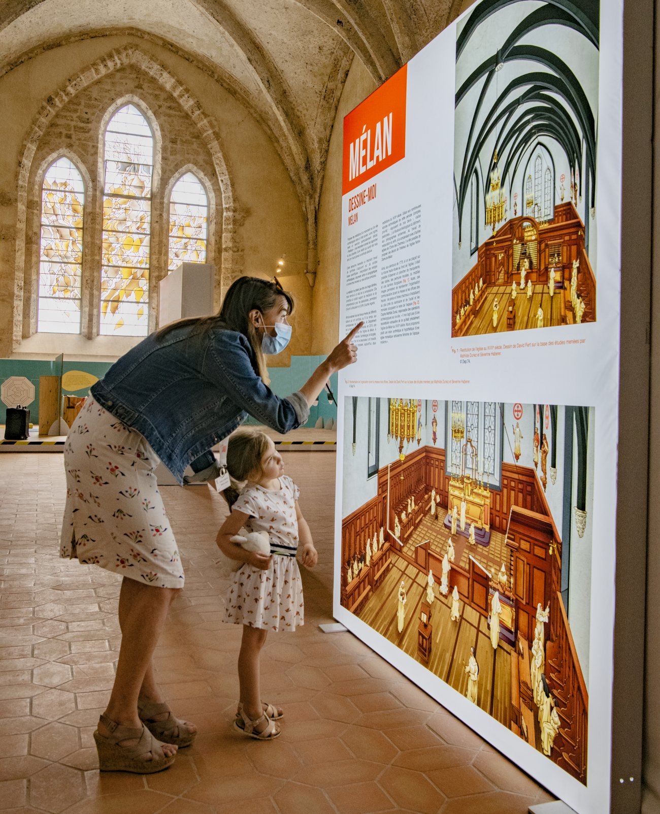 Une mère et sa fille regardent un panneau de l'exposition "Mélan, passé à la loupe". Morceaux choisis d'archéologie"