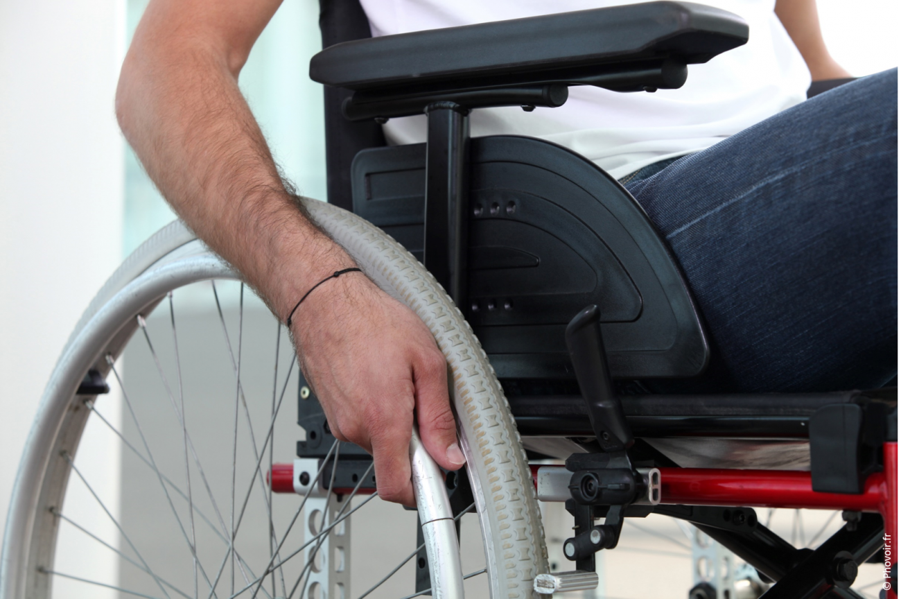 Handicap moteur : gros plan sur une main posée sur la roue d'un fauteuil roulant