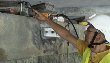 Homme portant un casque et montrant un appareil de mesure sous un pont