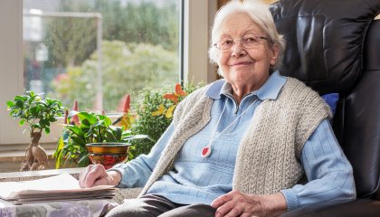 Une femme âgée est assise dans un fauteuil et porte le bouton de téléalarme autour du cou.