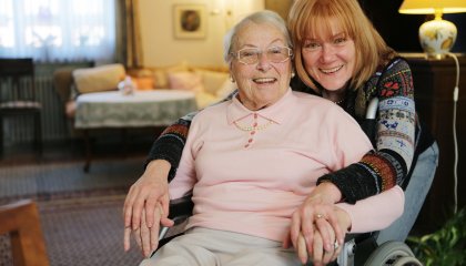 Une femme âgée est assise dans un fauteuil roulant et une femme plus jeune la tient dans ses bras.