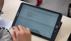 Un élève écrit un texte sur une tablette dans le cadre d'un atelier à l'éducation aux médias et à l'information.