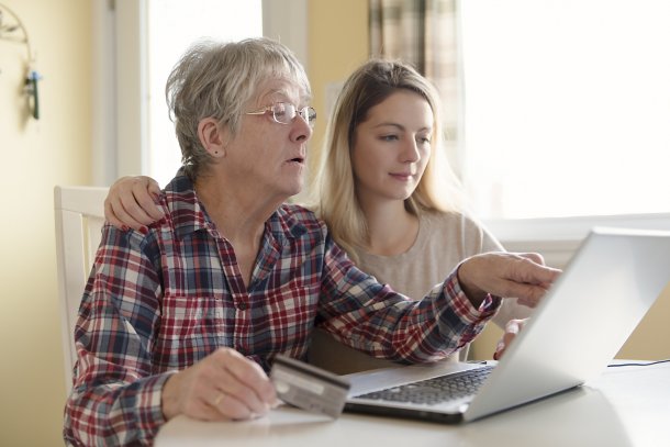 Une femme âgée et une jeune femme sont assises à une table, devant un ordinateur portable.