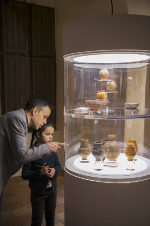 Un père montre à sa fille des céramiques antiques dans une vitrine.